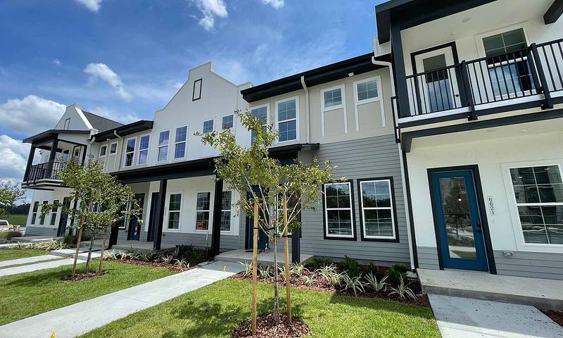 Row of modern townhouses with small front lawns and young trees. Sky is blue with scattered clouds.