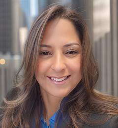 Portrait of a person with long hair smiling in an outdoor urban setting with tall buildings in the background.