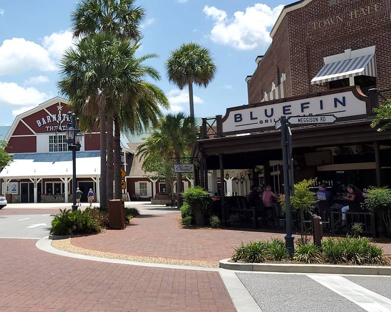 Outdoor view of Bluefin Grill and Bar beside palm trees, with Barnstorm Theater in the background under a clear blue sky.