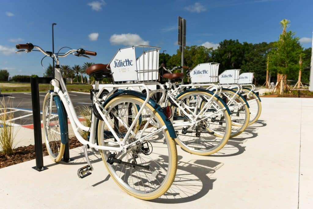 Row of white bicycles with baskets parked at a bike rack on a sunny day.