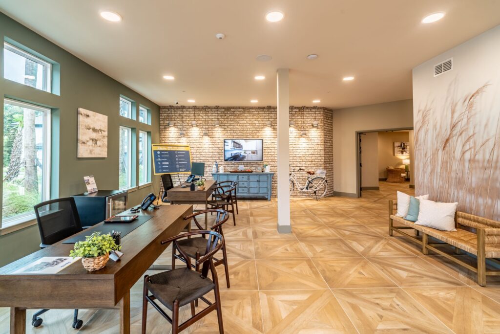 Modern office space with wooden flooring, desks, chairs, plants, a TV on a brick wall, and a bicycle. Soft lighting and neutral decor create a welcoming atmosphere.