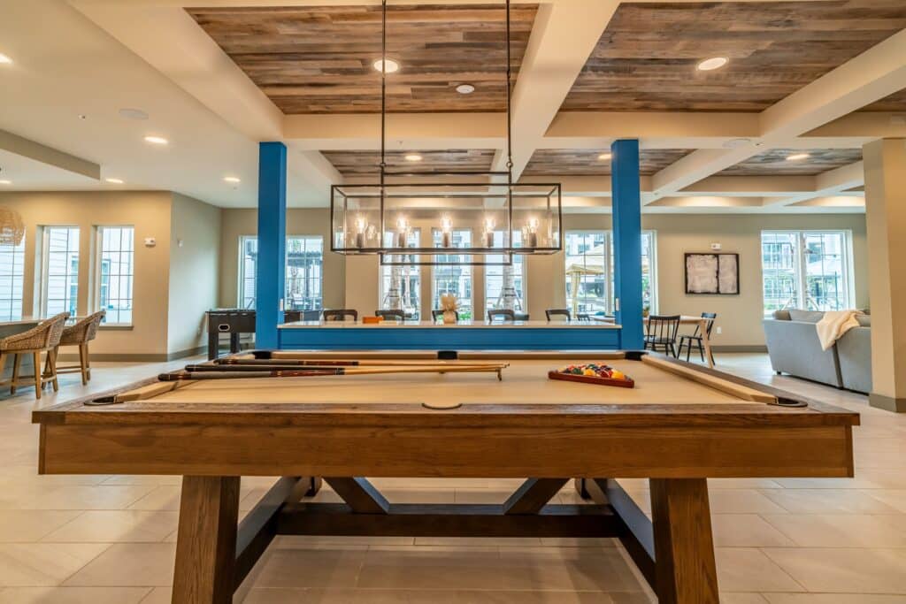 Luxurious game room with a wooden billiards table, modern chandelier, and seating area with a view of large windows.