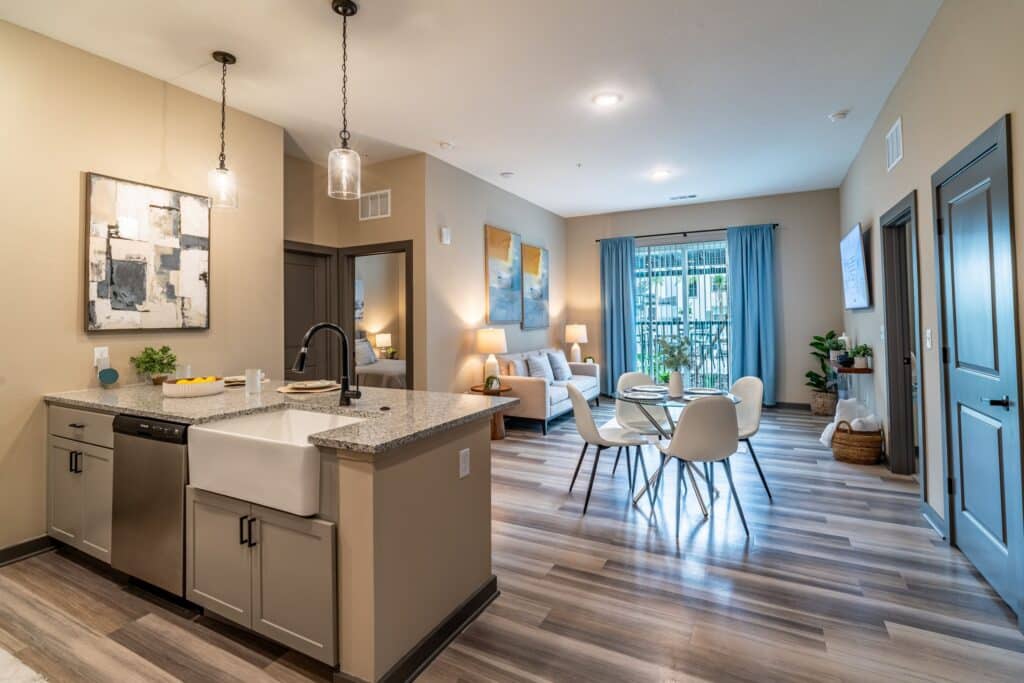 Modern open-concept kitchen and living area with granite countertops, dining table, blue curtains, and wood flooring.