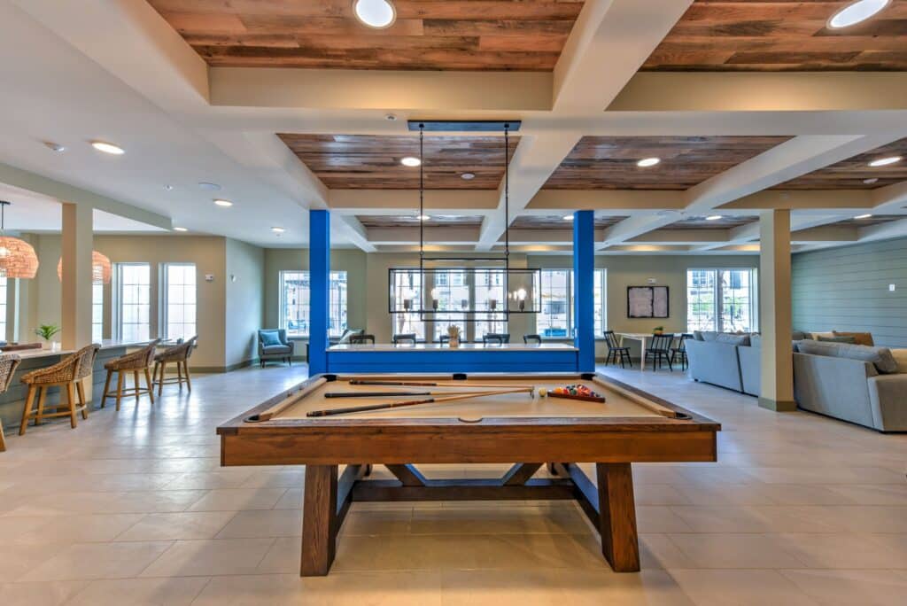 A modern communal space featuring a billiards table, seating area, and large windows letting in natural light.